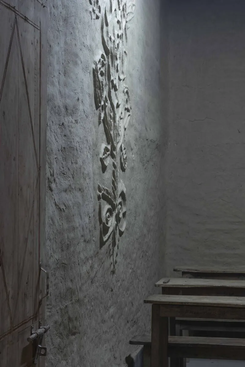 Detail of textured plaster wall with embedded impressions beside timber benches in shadowed light