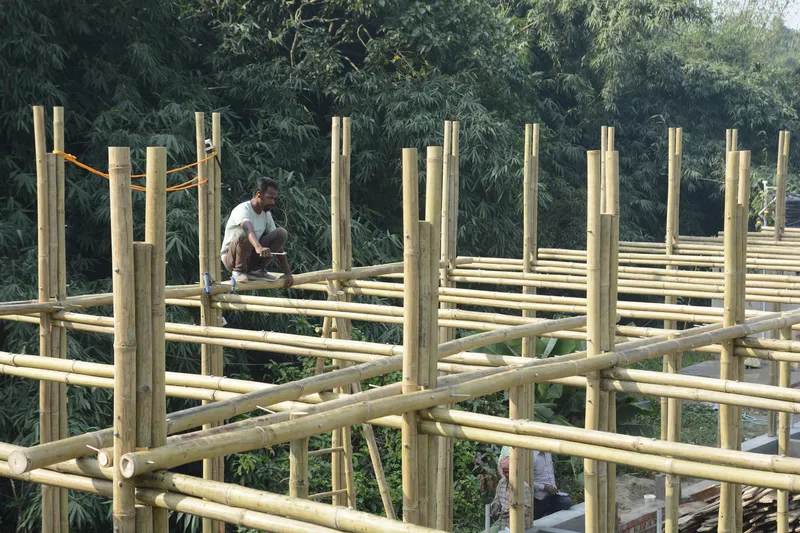 Worker crouching on the bamboo floor grid amid vertical columns and dense foliage beyond