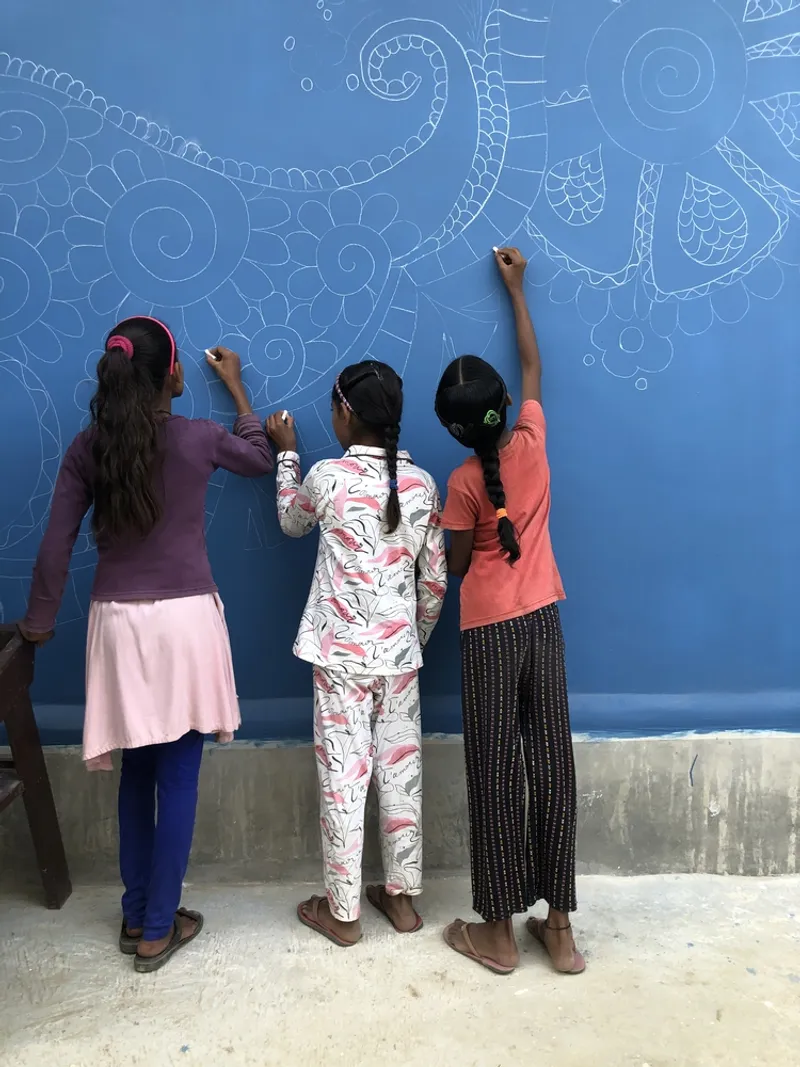 Three children drawing white line patterns on a bright blue painted exterior wall
