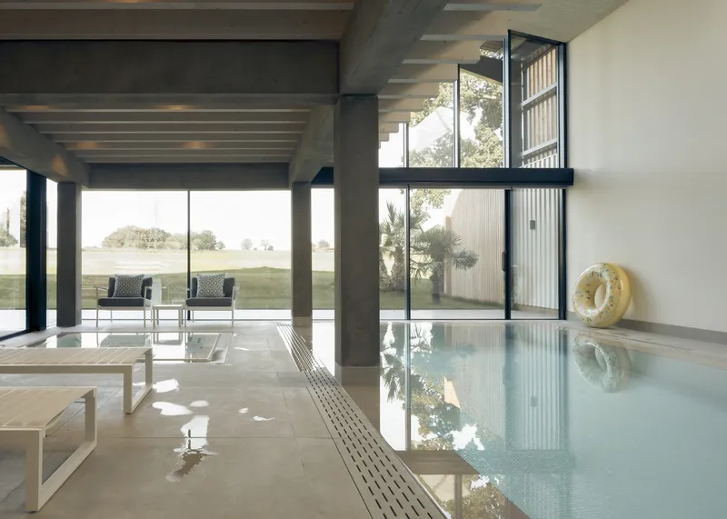 Indoor pool with tile edge and drainage channel beside glass walls opening to landscape with palms