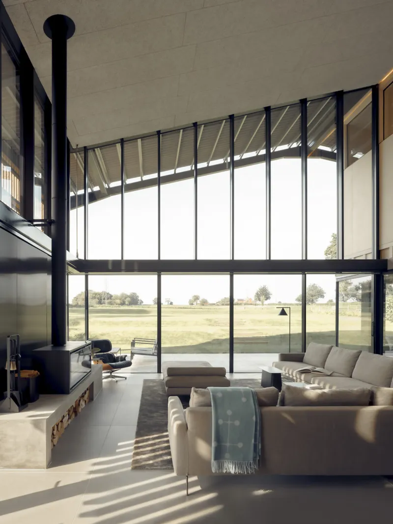 Double-height living space with floor-to-ceiling glass wall and freestanding black stove under concrete ceiling beams