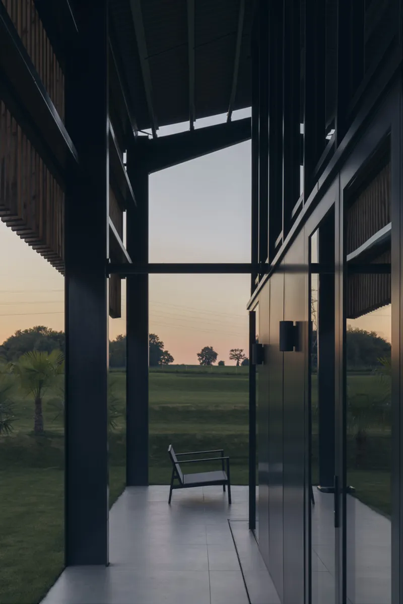 Covered terrace at dusk with exposed steel columns and clerestory window framing the darkening fields beyond