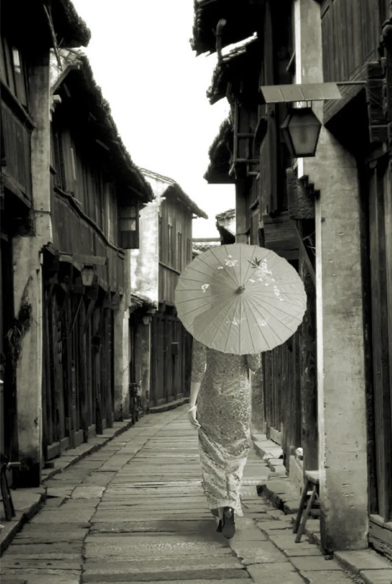 Narrow paved alley between timber houses with a figure holding a parasol walking away