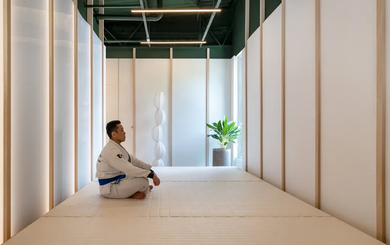 Person seated on light timber floor within translucent backlit panels framing a meditation space