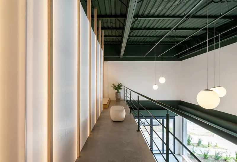 Upper-level corridor with polished concrete floor and backlit translucent wall panels beside mezzanine balustrade