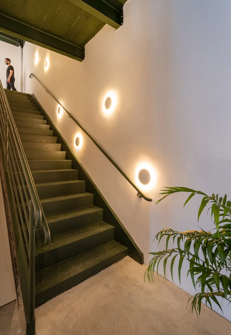 Steel staircase with round wall sconces lighting the white wall beside a potted plant