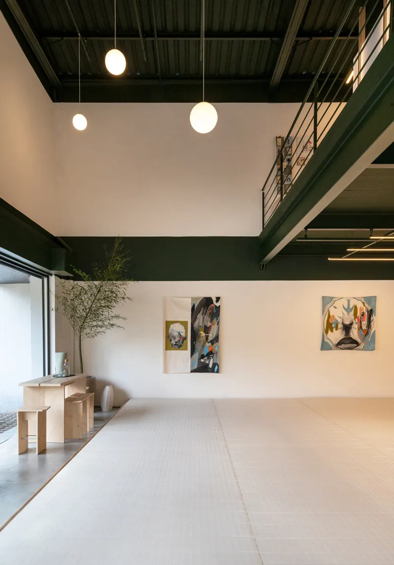 Double-height space with exposed green ceiling beams, tatami mat flooring and artworks on the wall