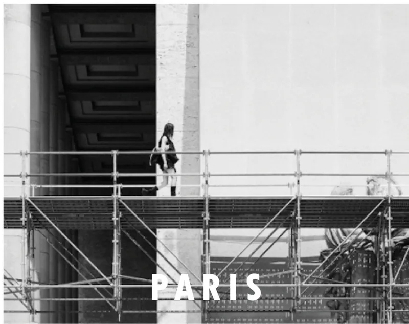 Exterior concrete wall with recessed opening and metal scaffolding as a woman walks across the platform