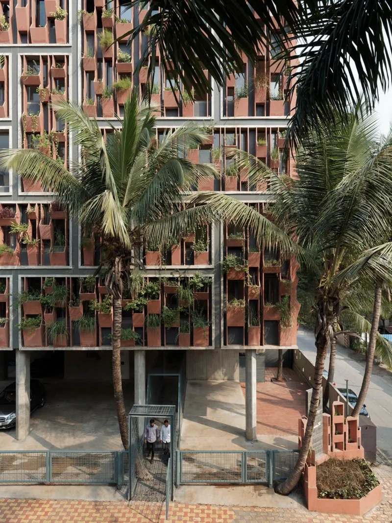 Facade with terracotta planters and integrated greenery behind palm trees and a wire mesh gate at ground level