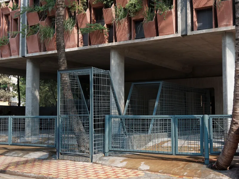Ground floor entry with diagonal wire mesh gates and exposed concrete columns beneath planted balconies