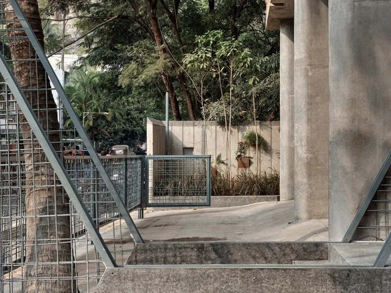 View through diagonal steel bracing toward courtyard with wire mesh gate and planted concrete planters