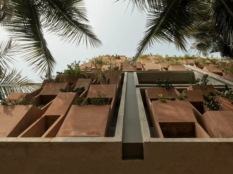 Upward view of the terraced concrete facade with planted balconies framed by palm fronds overhead