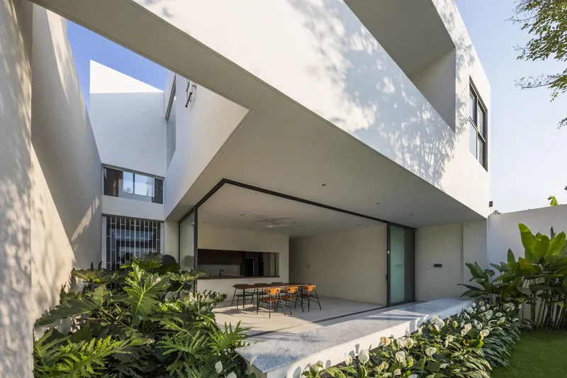 Covered terrace opening to planted courtyard with dappled tree shadow across white plaster walls