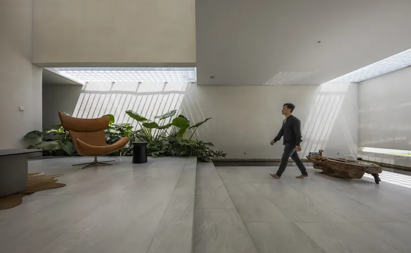 Interior gallery space with person walking past planted beds beneath angled translucent skylights