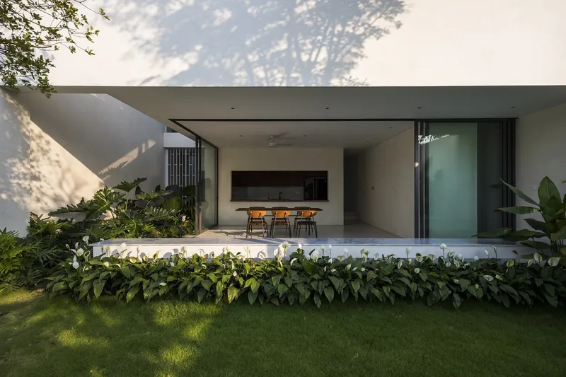 Covered dining terrace with planted beds and lawn under dappled tree shadow at dusk