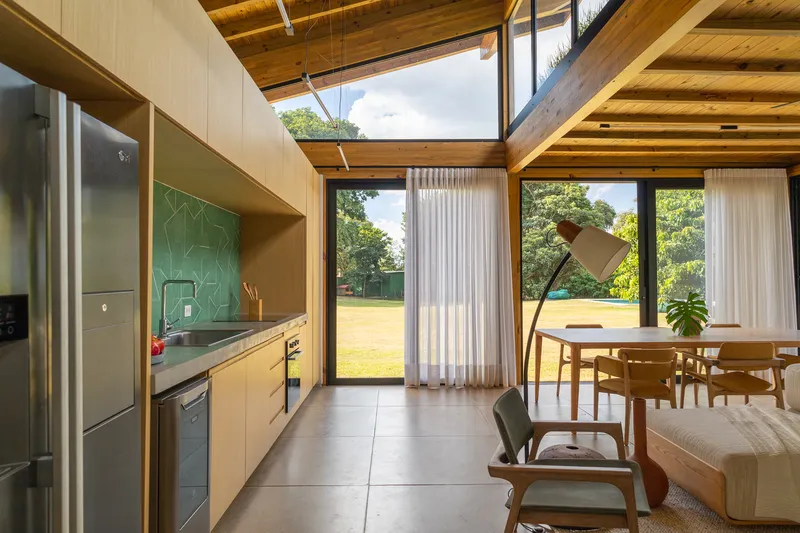 Kitchen and dining area with floor-to-ceiling windows framing views of the surrounding lawn and trees