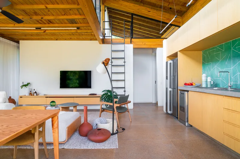 Open-plan living space with exposed timber ceiling beams and a steel ladder accessing the loft above