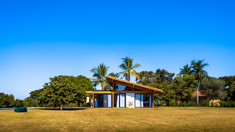 Glass-walled pavilion beneath an angled roof set against palm trees and a clear blue sky