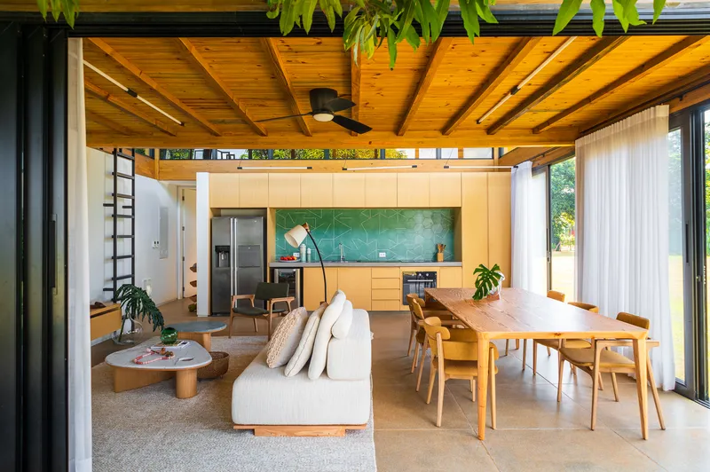 Open plan living and dining space with exposed timber ceiling and green tile kitchen backsplash
