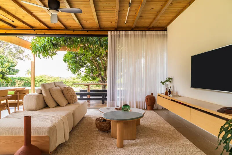 Living area with timber ceiling and floor-to-ceiling sheer curtains opening to garden terrace