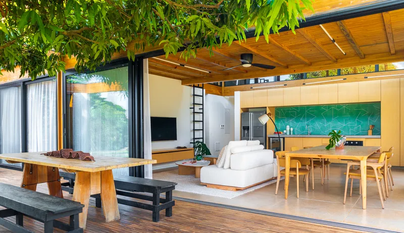 Interior opening to timber deck with dining table beneath overhanging tree branches