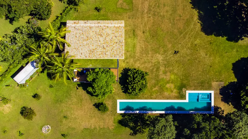Drone view of the tiled roof pavilion and rectangular pool surrounded by palms and grassy site