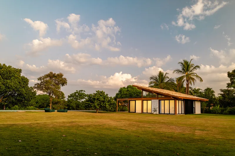 Single-volume pavilion with sloped roof and full-height glazing set in an open lawn surrounded by palm trees