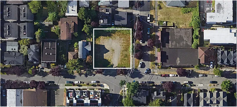 Aerial view of a vacant corner lot outlined in white among surrounding buildings and parked cars