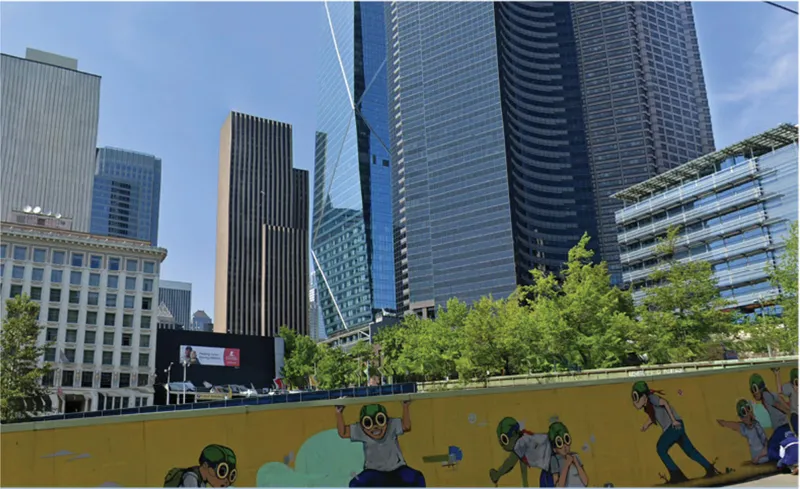 Yellow hoarding barrier with painted figures along a sidewalk with high-rise towers behind