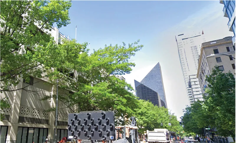 Street view of a perforated black screen wall with trees and pedestrians in the foreground