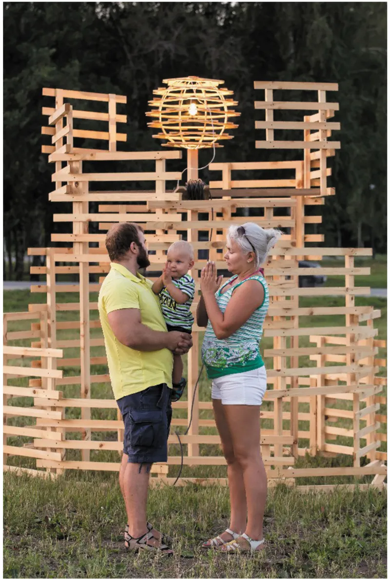 Family of three standing before the illuminated spherical lantern at the center of the timber pavilion