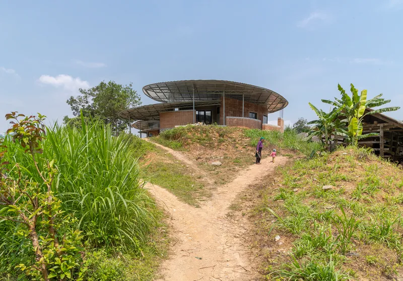 Dirt path ascending through wild grasses toward the circular roof structure with two figures climbing