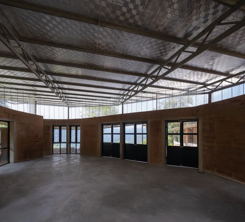 Interior room with rammed earth walls and hexagonal tiled ceiling visible through steel trusses overhead
