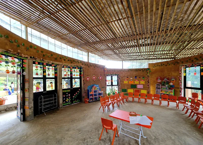 Classroom with curved timber slat ceiling, rammed earth walls, and orange plastic chairs arranged in rows