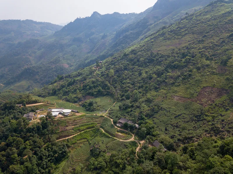 Aerial view of terraced hillside site with curved roof buildings nestled among rice paddies and forest
