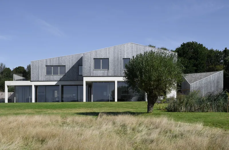 Garden facade with vertical timber cladding and white render base seen across dry grass meadow