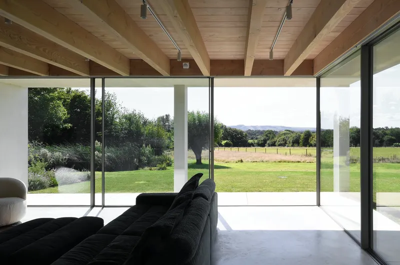 Living room with exposed timber beams and floor-to-ceiling glass doors opening to a green lawn