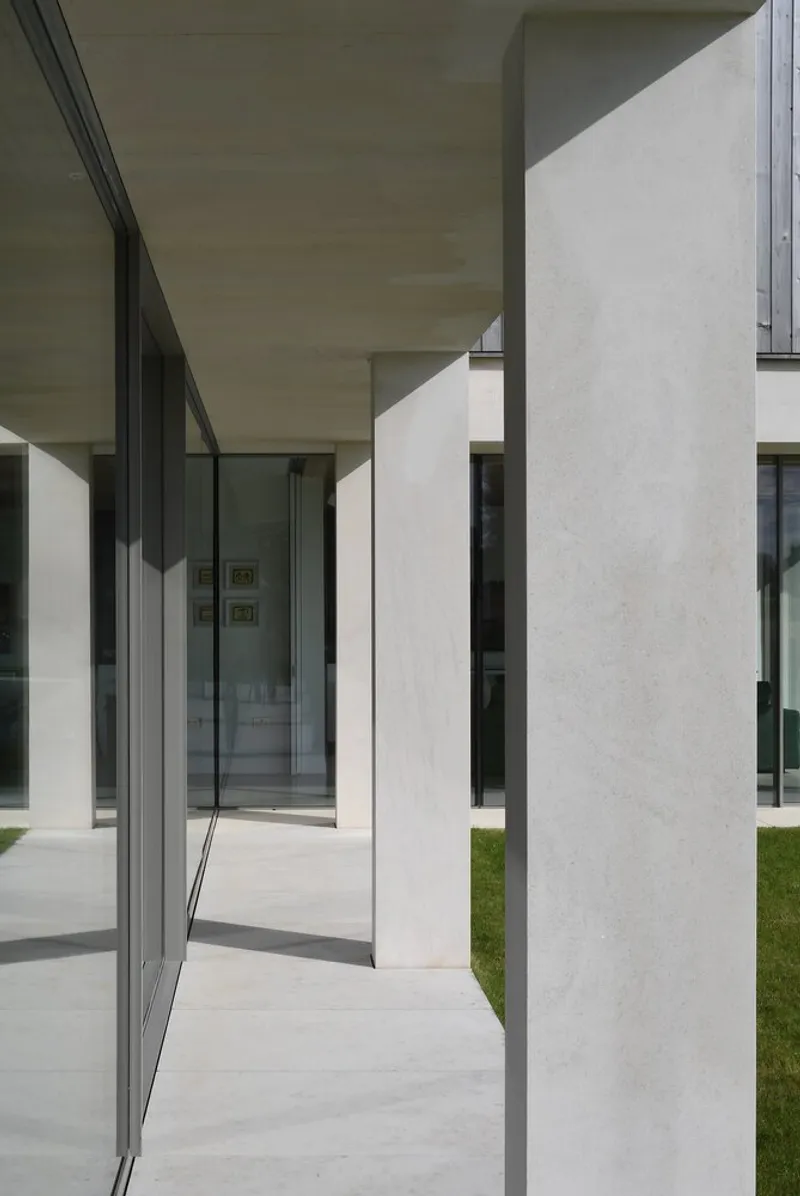 Covered walkway framed by white plaster columns and timber soffits casting hard shadows in daylight
