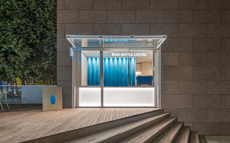 Frontal view of glass kiosk with open folding doors against brown masonry wall