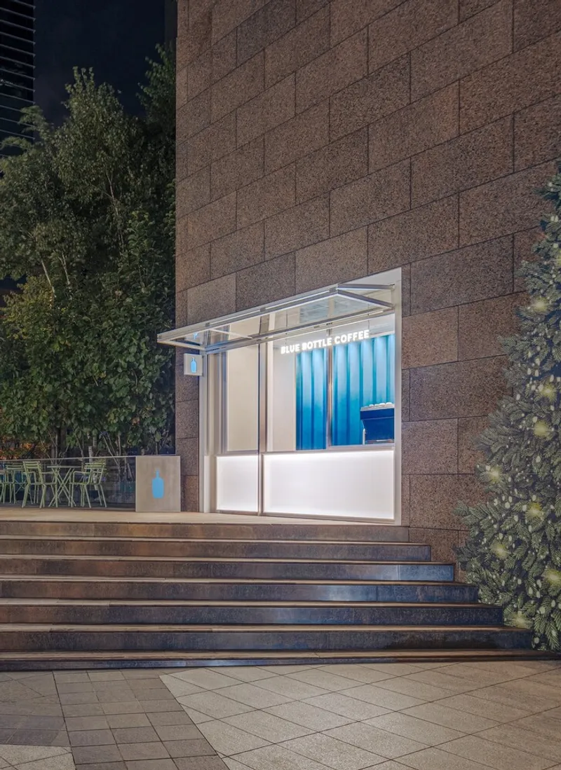 Glass kiosk with white canopy and blue striped interior against a textured stone wall