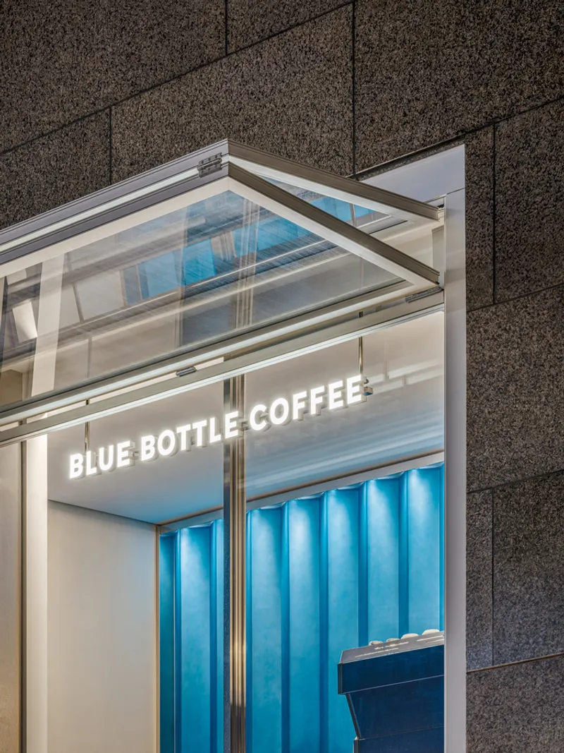 Close-up of the glazed canopy corner and illuminated signage above blue striped panels