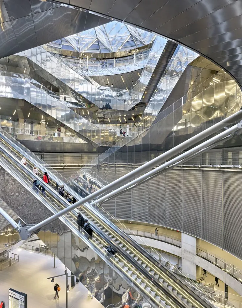 Interior void showing diagonal escalators framed by a reflective faceted skylight and perforated metal balustrades