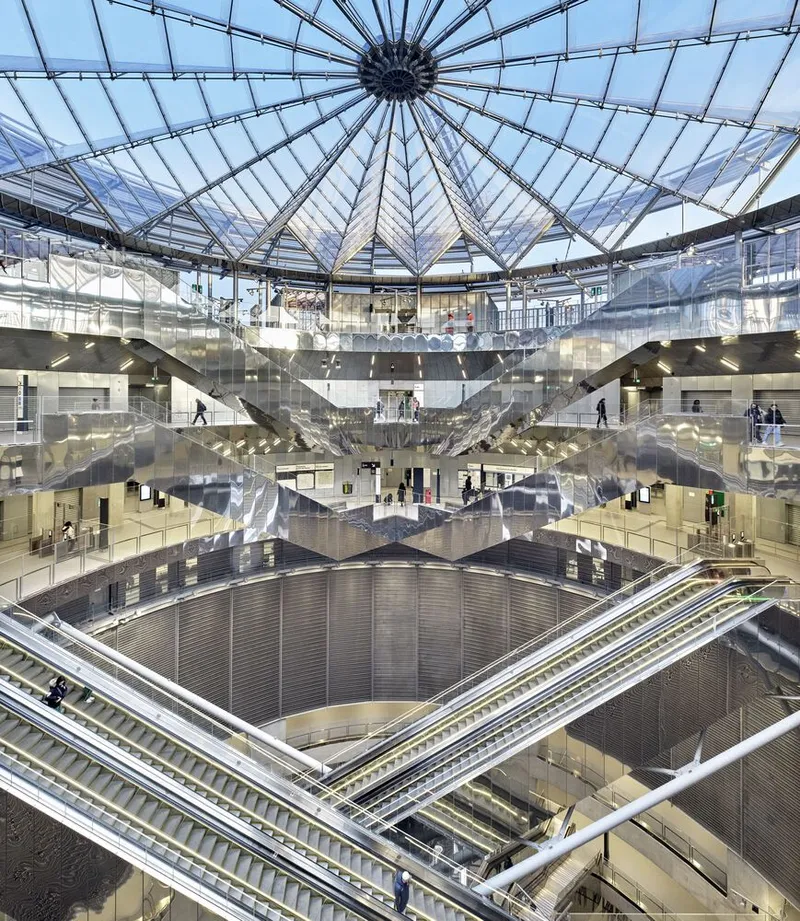 Multi-story atrium beneath a radial glass dome with intersecting escalators and reflective curved ceiling panels