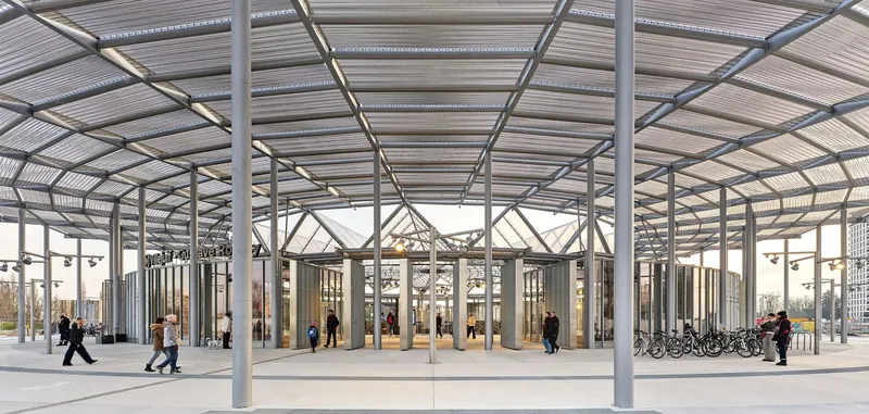 Covered canopy with exposed steel columns and corrugated roof sheltering pedestrians and bicycles outside