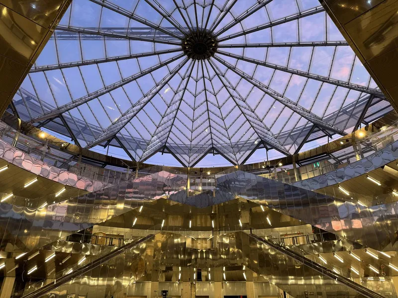 Radial glass skylight with steel ribs converging at a central hub framed by reflective metallic wall panels