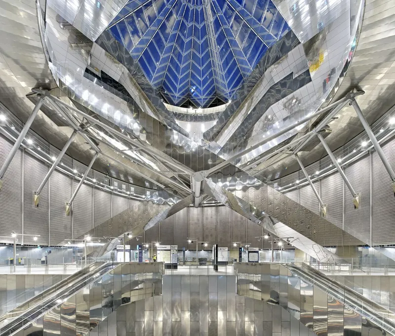 Symmetrical view of the faceted atrium ceiling with diagonal escalators and polished floor reflecting the metallic surfaces