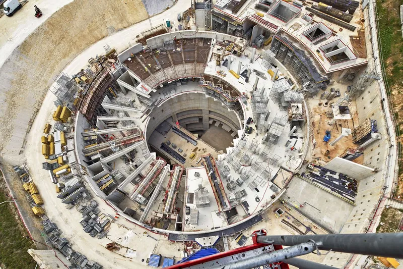 Aerial view of circular excavation pit with concentric concrete rings and construction equipment scattered around perimeter