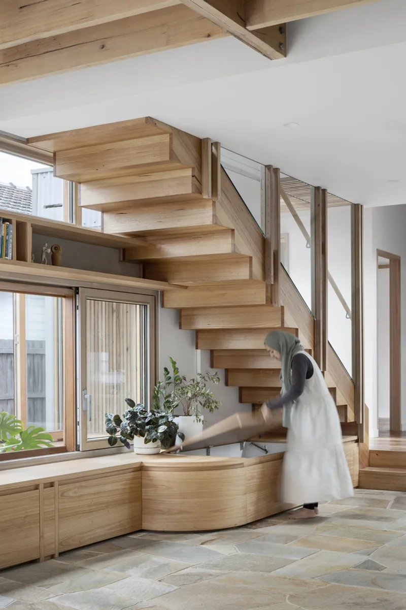 Floating timber staircase beside a curved built-in bench with a person in motion and potted plants below