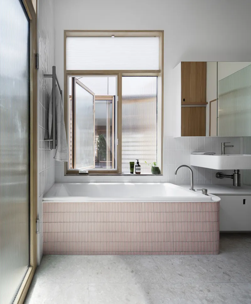 Bathroom with pink mosaic-tiled tub surround and timber-framed window opening to a courtyard
