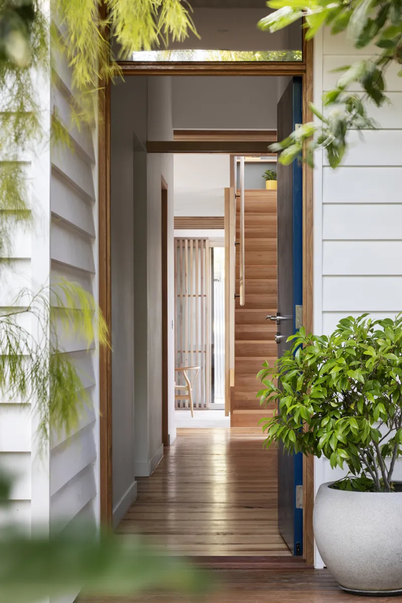 Entry doorway framed by white weatherboard cladding and overhanging foliage in dappled sunlight